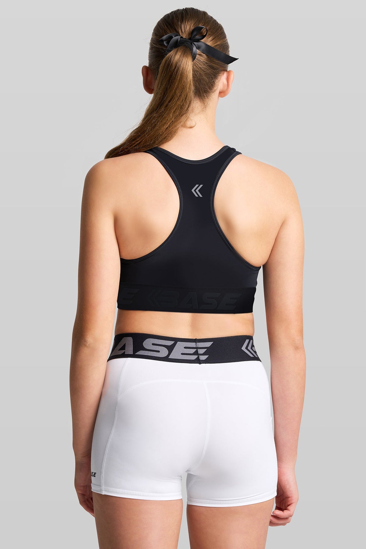 Person wearing a black sports bra and white shorts with a visible brand logo on a gray background