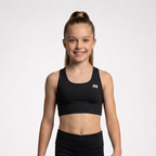 A young girl with her hair in a high ponytail smiles while wearing a black athletic crop top and matching black leggings against a light gray studio background. The crop top features a small white 'RS' logo on the left chest.