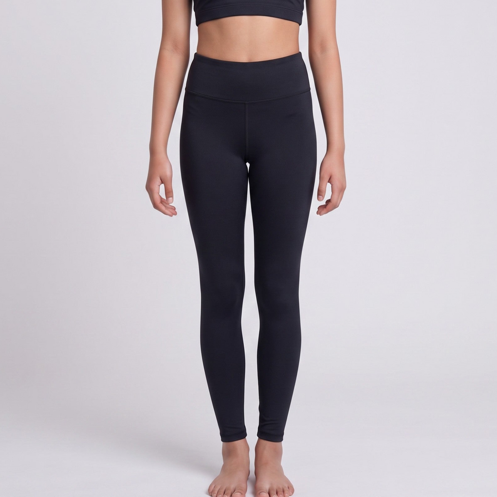 A model wearing black high-waisted leggings and a matching black sports bra, standing against a light gray studio background.