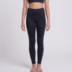 A model wearing black high-waisted leggings and a matching black sports bra, standing against a light gray studio background.