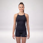 A woman modeling a black athletic tank top and matching black shorts against a light gray studio background. The shorts have a small white logo on the lower left leg.
