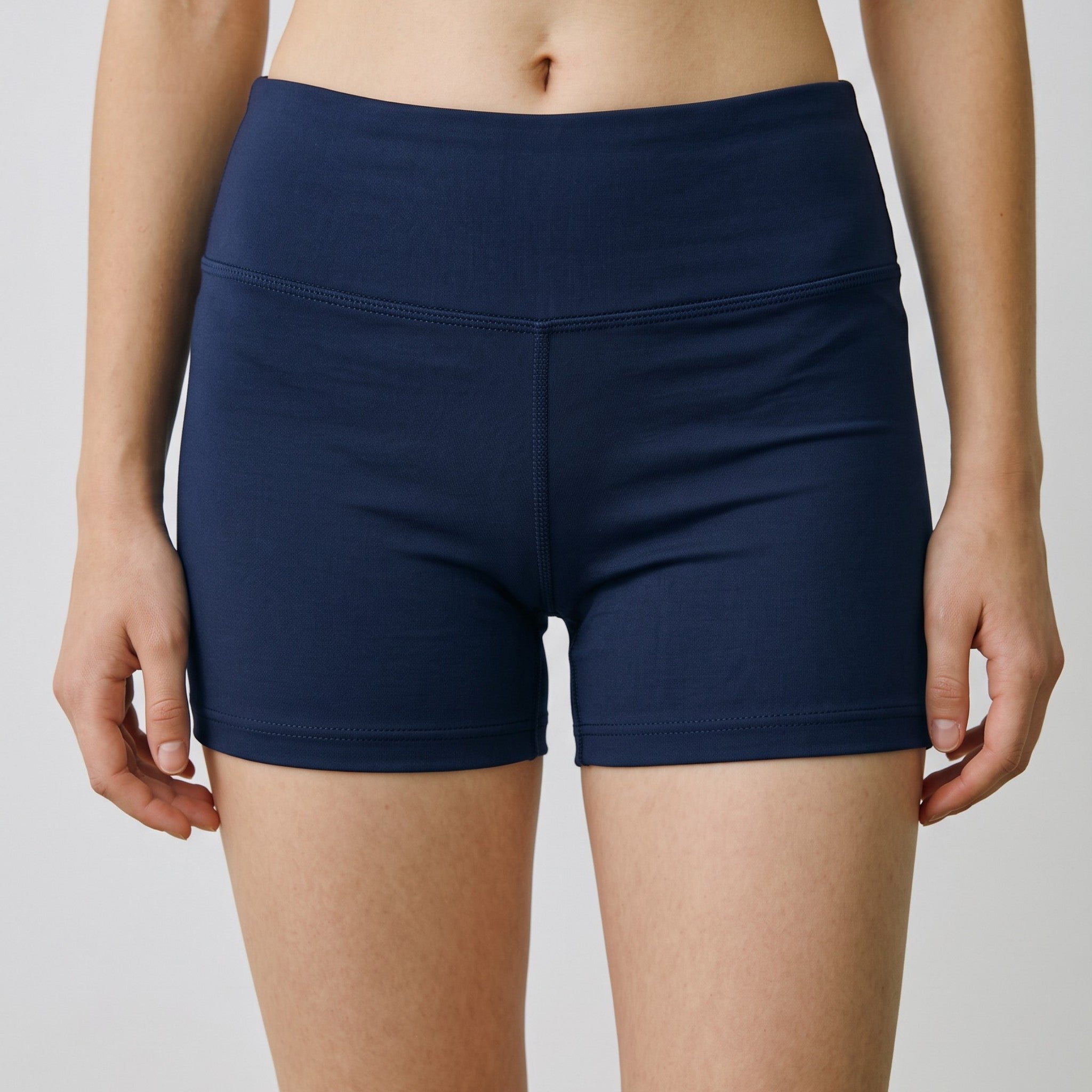 A close-up of a model wearing high-waisted navy blue athletic shorts against a light gray studio background.